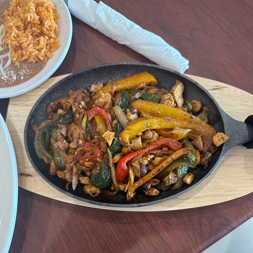 Sizzling chicken fajitas with colorful bell peppers and onions in a cast iron skillet, with rice and beans.