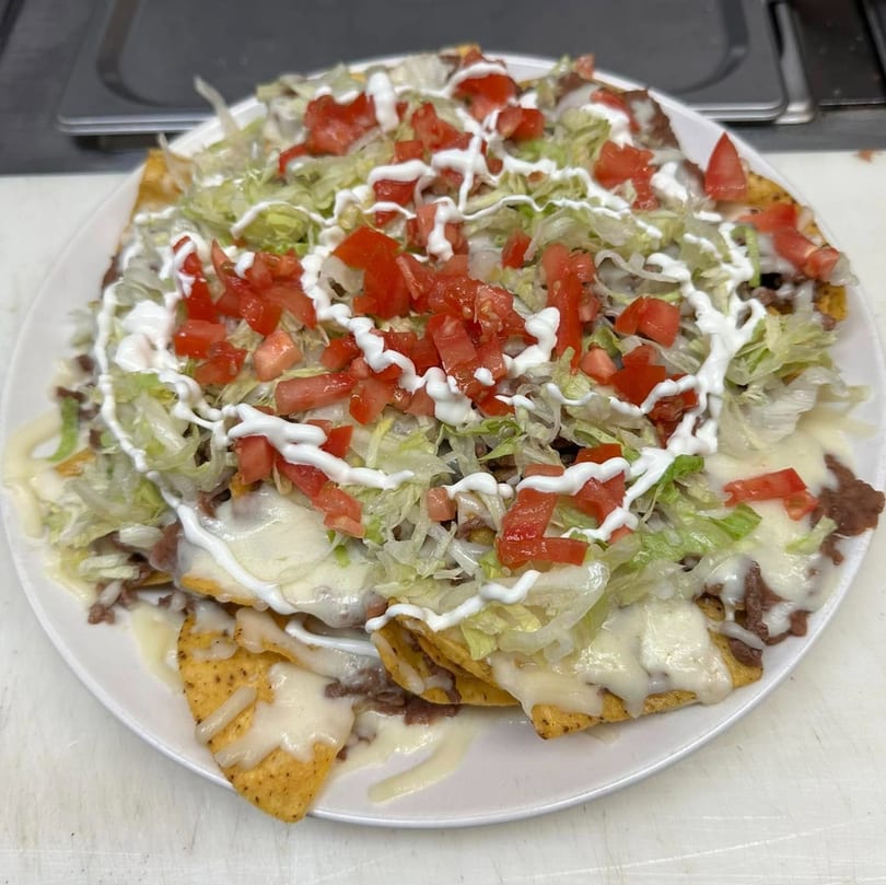 A large plate of nachos with melted cheese, ground beef, shredded lettuce, diced tomatoes, and sour cream.